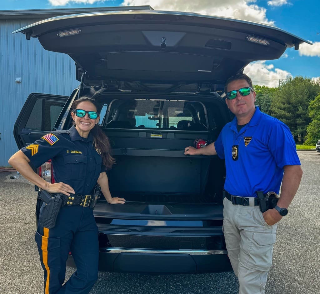 Two people alongside the open rear equipment compartment of an SUV